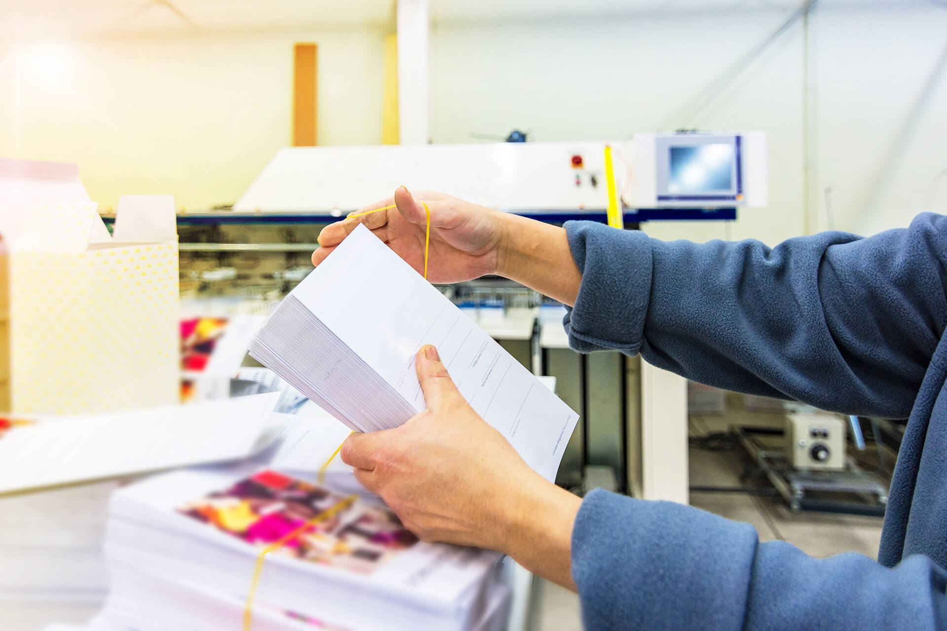 A person examines a stack of printed sheets, preparing them for packaging in a print production facility.
